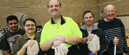 group of smiling men with mops in a warehouse