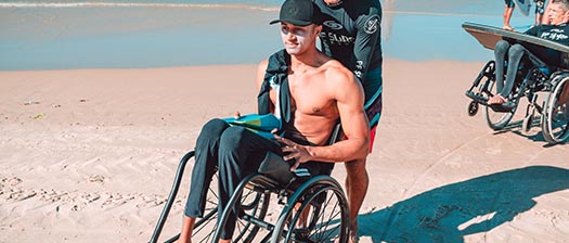 young man on beach with no shirt being pushed in a wheelchair