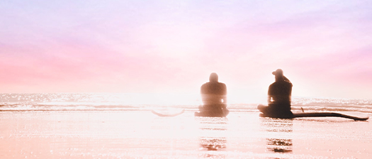two people sitting on beach bathed in pastel morning light