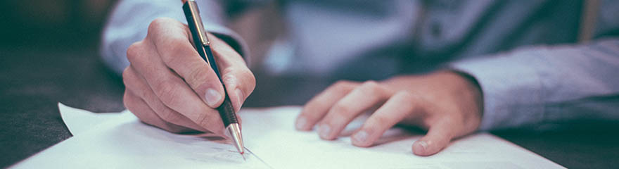 A man sits at a desk with a pen, writing on a document
