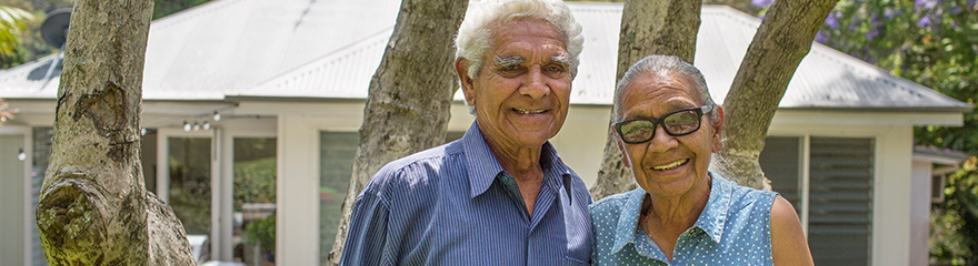 A senior couple stand and smile outside a house