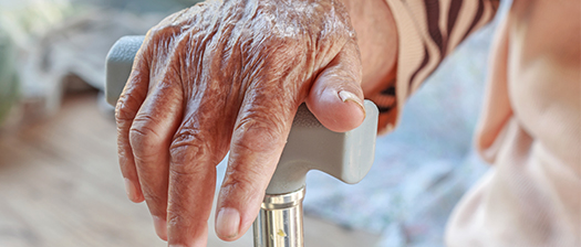 Close up of an elderly hand resting on a walking cane