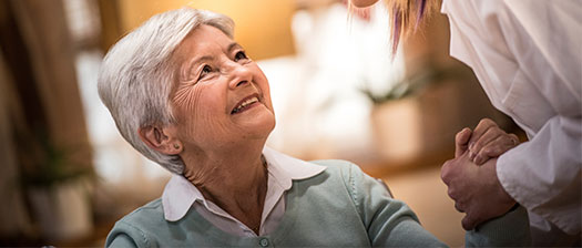 A senior woman looks up and smiles at a caregiver.