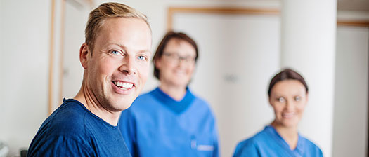 Three people in blue scrubs smiling towards camera