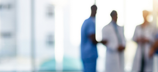A blury image of three people standing in the distance of a health facility, they are wearing long white coats and medical scrubs