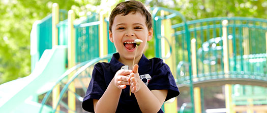 A young child playing in a playground, they are holding a flower in front of them and smiling towards the camera