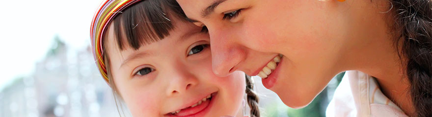 Close up of young person with disability smiling towards the camera together with their support person