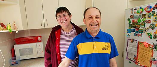 Two people with disability standing smiling in the kitchen of a supported disability accommodation