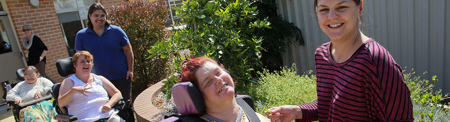 People with disability using mechanical wheelchair alongside their support people in an outdoor garden setting