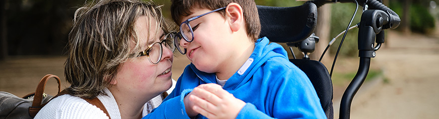 Young person in wheelchair cuddling up to the parent or carer who is crouched down next to them.