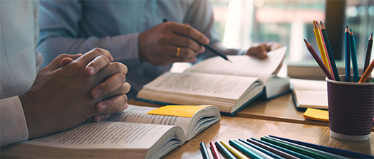 Desk view of two people studying side by side with books open and pencils near by