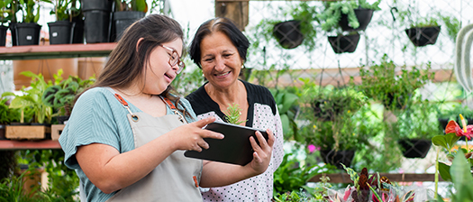 Two people stand in a plant nursery looking at a tablet.