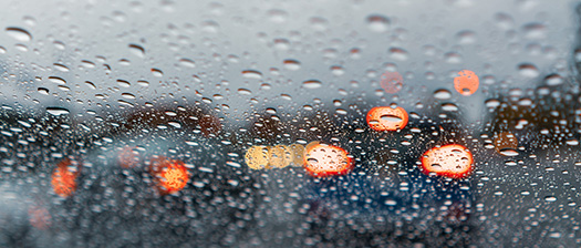 Out of focus image of rain on windscreen with car lights in background
