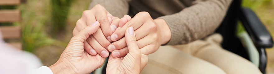 Close up of two people holding hands in support while they sit opposite each other