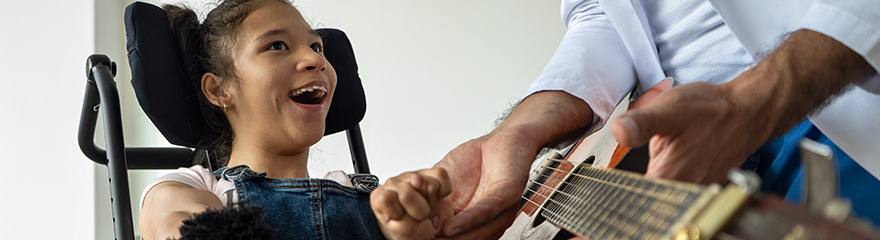 A young woman with disabiltiy smiles at a man playing guitar.