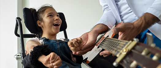 A young woman with disabiltiy smiles at a man playing guitar.