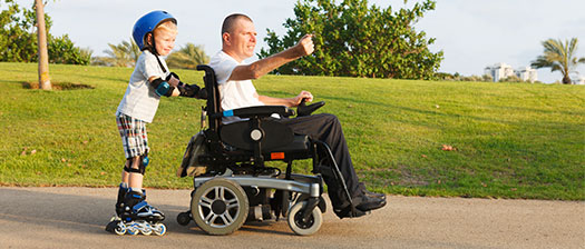 Child using roller skates pushing an adult's wheelchair through a park