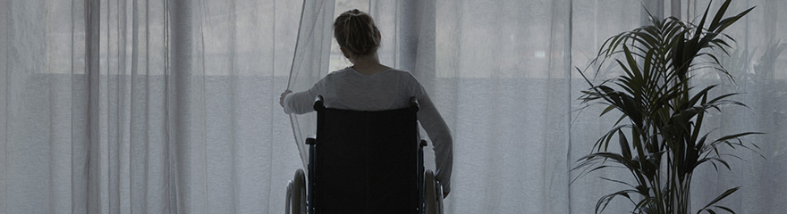 Rear view of person in wheelchair looking through curtains