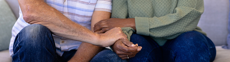 Two people holding hands in support while sitting on a couch