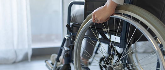 A close up image of a person holding the wheel of a wheelchair. They are in a room looking out a window