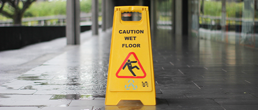 Outside a building a pathway has a yellow sign on it that says caution wet floor. 