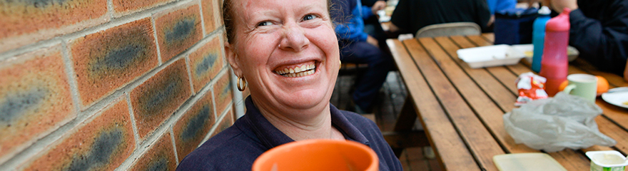 A worker holding a smiling face mug up to the camera and grinning.