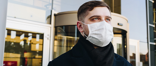 Person with white mask stares into the distance, they are standing in front of an office building