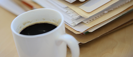 A cup of coffee sits next to a folder of papers