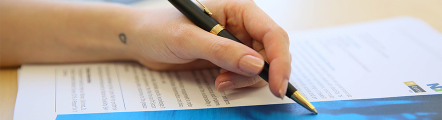 Hand holding a pen pointing to documents on a desk  