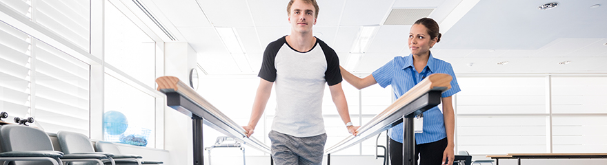 Allied health professional assisting an individual walking with bars in a clinical setting