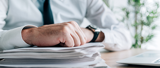 A person in a business shirt leans on a stack of papers