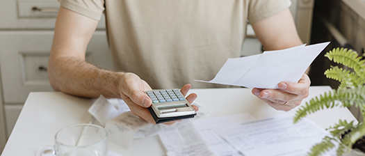 Close up of a person holding a calculator in one hand and paperwork in the other