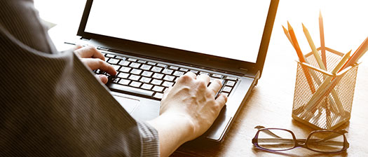 Close up of person sitting at an office desk. They are typing on a laptop.