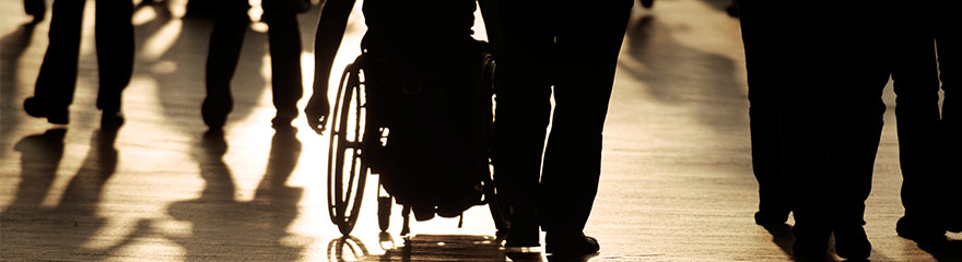A floor level image of a crowd that show legs and a wheelchair in silhouettes and shadows