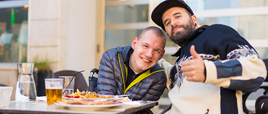 Person with disability sitting at a cafe table enjoying food with their support person.