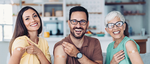 three smiling people show medical plasters on their shoulders