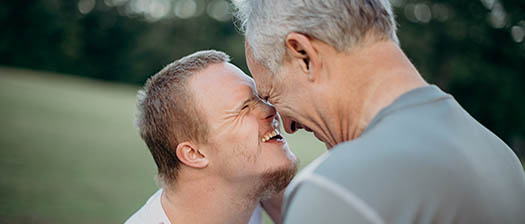 smiling young man and older man embrace on tennis court