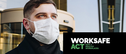 Person wearing a surgical mask standing outside an office building. Worksafe ACT logo